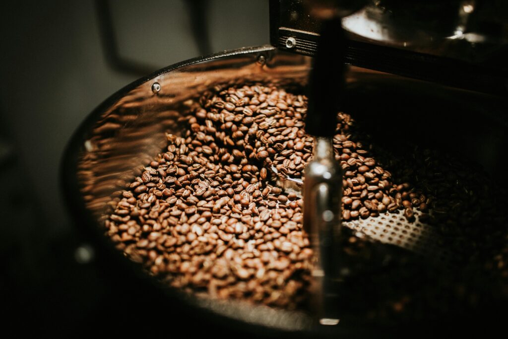 Close-up of roasted coffee beans inside a roasting machine with a metal stirring arm. | Hustle Coffee