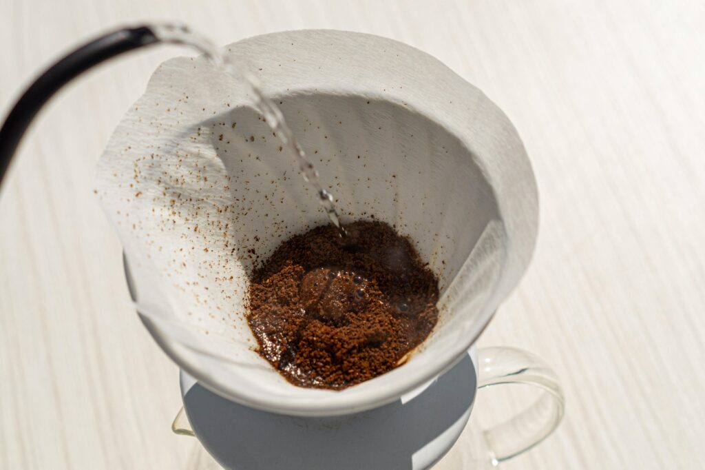 Water being poured over ground coffee in a paper filter for brewing, with a glass carafe below. | Hustle Coffee