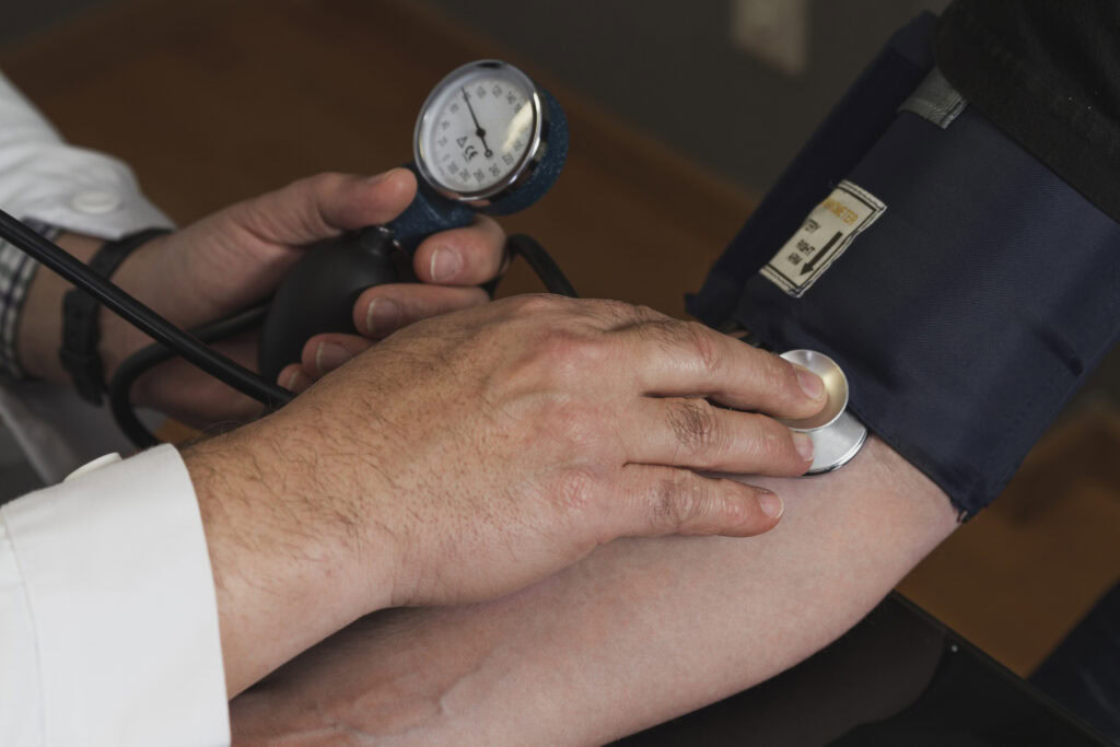 Close-up of a healthcare worker measuring a person's blood pressure with a sphygmomanometer and stethoscope. | Hustle Coffee