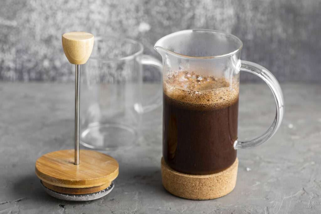 A French press with brewed coffee and its plunger removed, sitting on a gray surface against a textured background. | Hustle Coffee