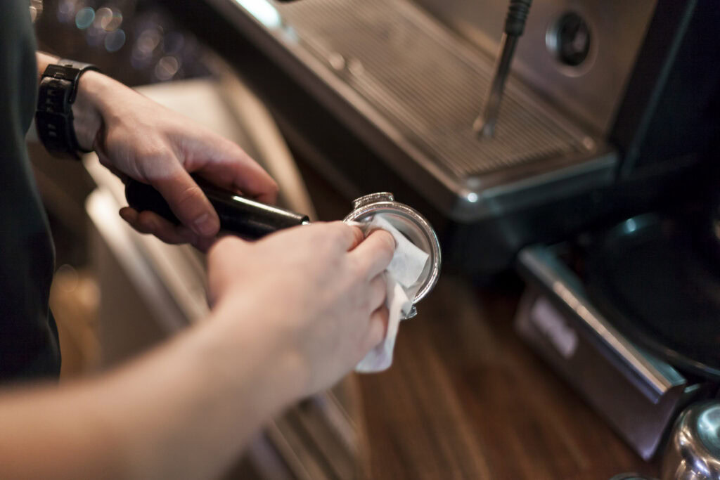 Close-up of a person cleaning a portafilter at a coffee machine in a café. | Hustle Coffee