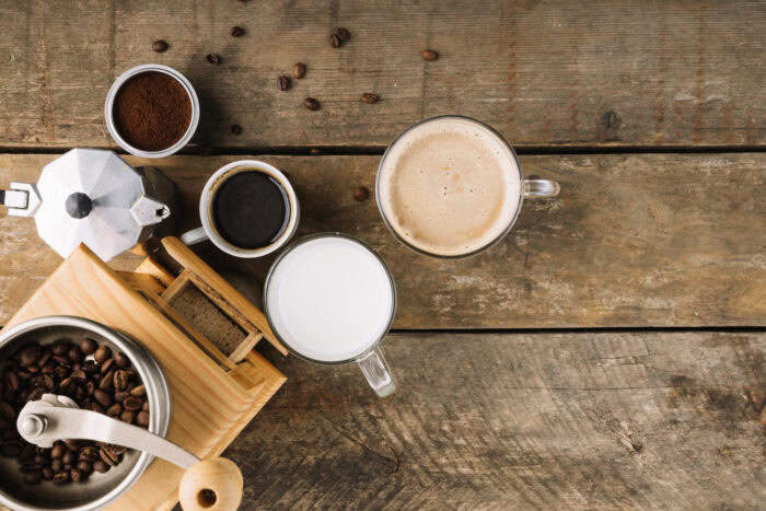 Top view of coffee beans, ground coffee, milk, espresso, cappuccino, and a moka pot on a rustic wooden table. | Hustle Coffee