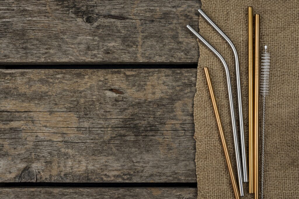 Metal straws and a cleaning brush on a piece of burlap next to a rustic wooden surface. | Hustle Coffee