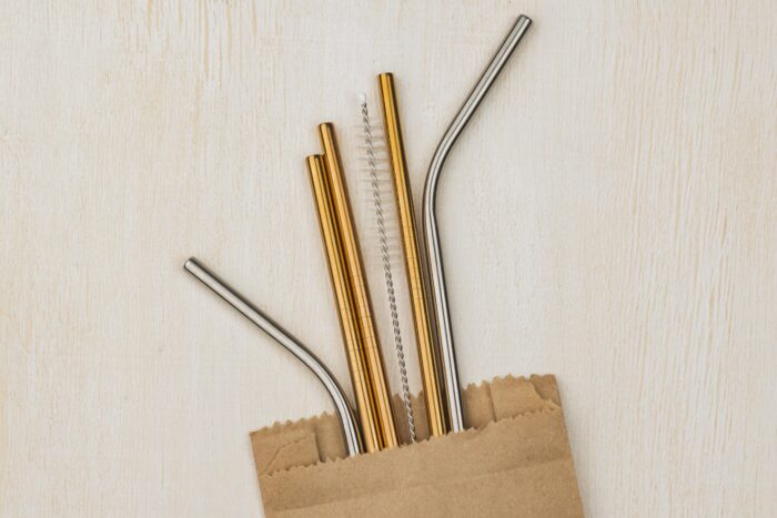 Metal straws and a cleaning brush in a brown paper bag on a light wooden surface. | Hustle Coffee