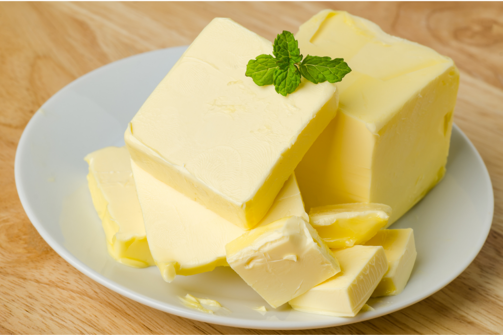 Several blocks and slices of butter on a white plate, topped with a sprig of fresh mint, on a wooden surface. | Hustle Coffee