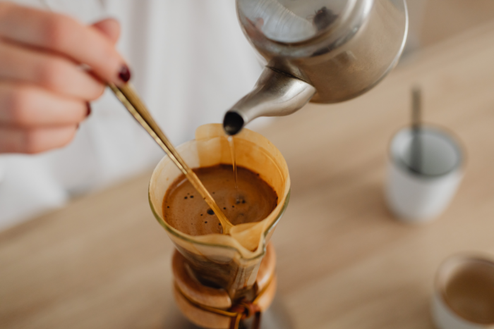 A person pours hot water from a kettle over coffee grounds in a Chemex with a paper filter. | Hustle Coffee