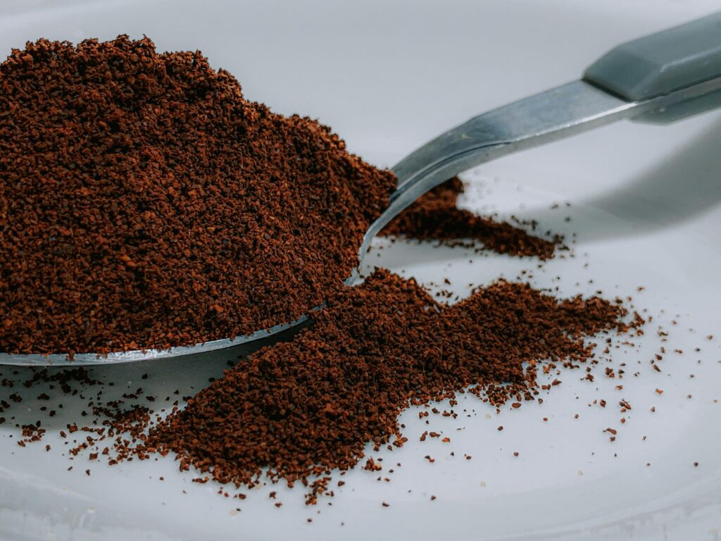 A close-up of ground coffee on a spoon and spilled onto a white surface. | Hustle Coffee