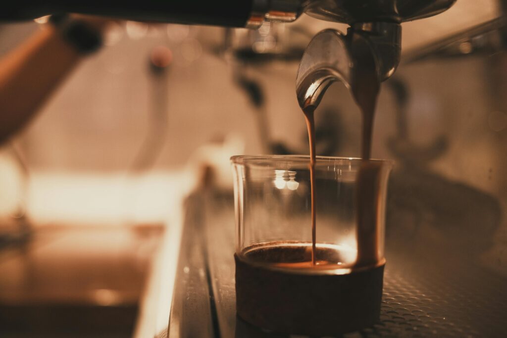 Close-up of espresso pouring from a machine into a clear cup, with a blurred background. | Hustle Coffee