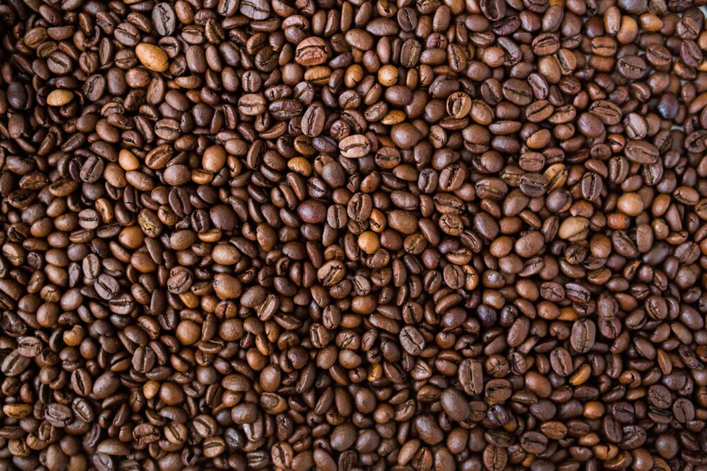 Close-up view of many roasted coffee beans densely packed together, showing various shades of brown. | Hustle Coffee