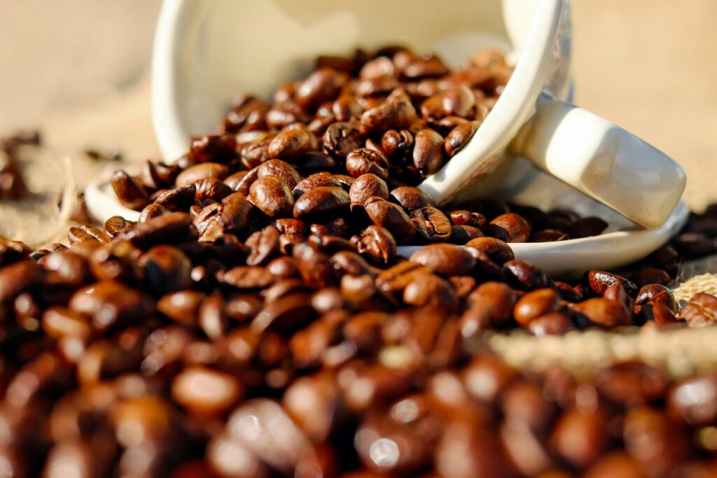 Glossy coffee beans spilling out of a white ceramic cup onto a burlap surface. | Hustle Coffee