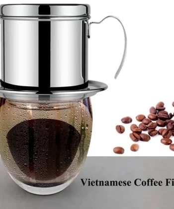 A Vietnamese coffee filter dripping coffee into a glass cup, with coffee beans scattered on the right. | Hustle Coffee