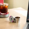 Reusable coffee pods filled with grounds sit on a wooden table next to a glass of iced coffee and a laptop. | Hustle Coffee